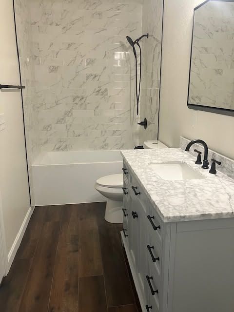 Modern bathroom with marble vanity, dark wood floor, and white tub-shower combo.