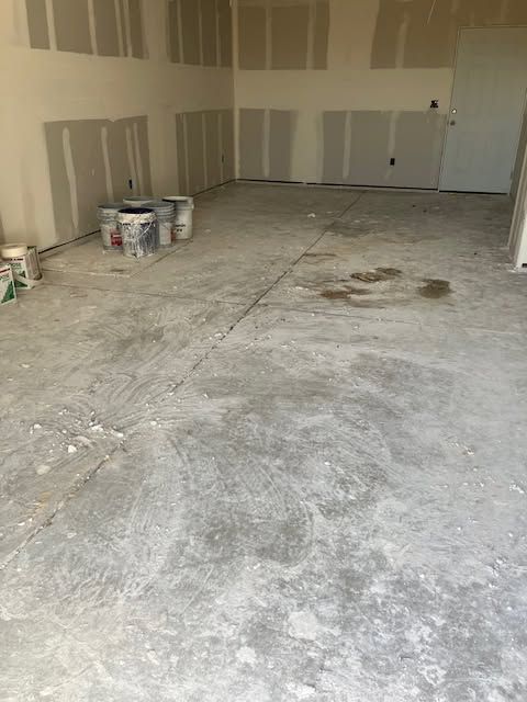 Empty unfinished garage with bare drywall, concrete floor, and paint buckets along the left wall