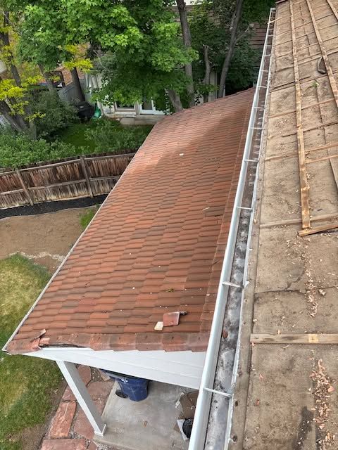 Steep red shingle roof beside a flat roof, viewed from above with trees and a yard below