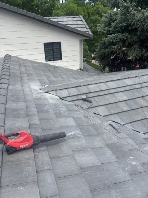 Roof shingles under repair with red leaf blower on gray shingled roof near a white house