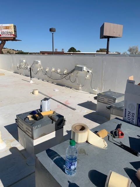 Rooftop work area with tools, wires, and a water bottle under bright daylight.