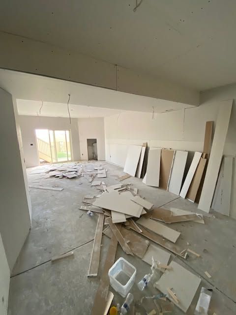 Messy interior room with construction debris, stacked boards, and unfinished walls near a bright window.