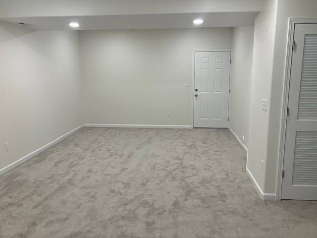 Empty beige living room with carpet, recessed lights, and white doors and walls