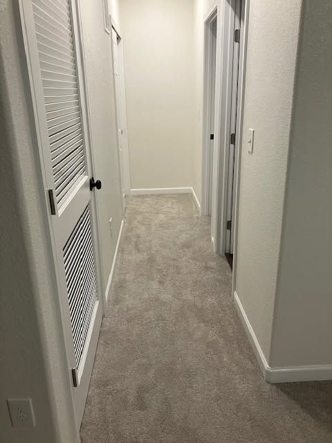 Narrow carpeted hallway with white walls and louvered closet doors, viewed toward a closed door.