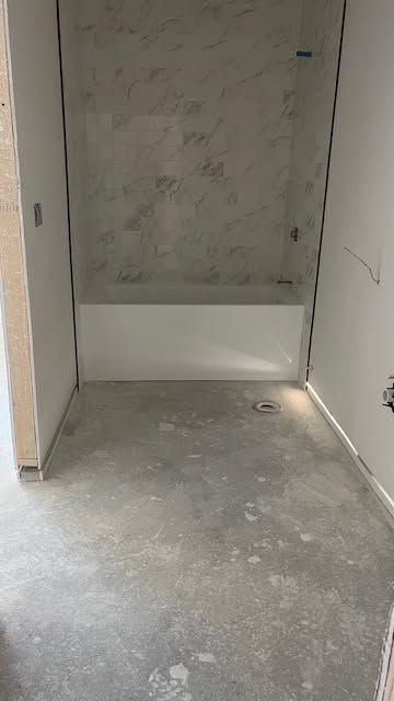 Empty unfinished hallway with gray concrete floor and white walls, showing a recessed alcove at the end.