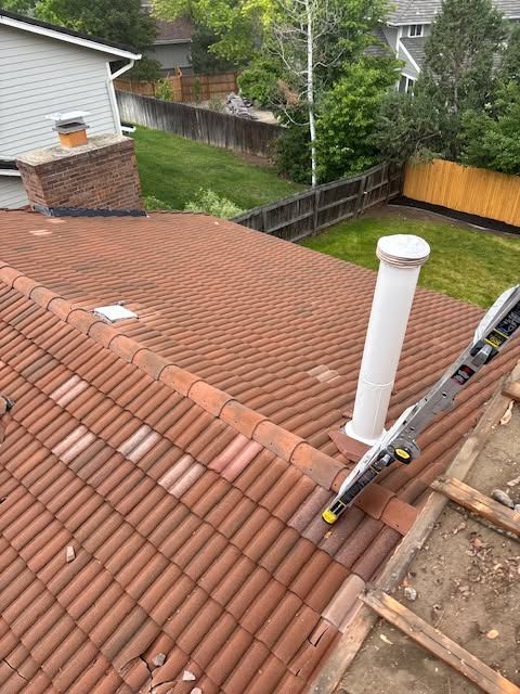 Rooftop view with red tiles, white vent pipe, ladder, and fenced backyard below