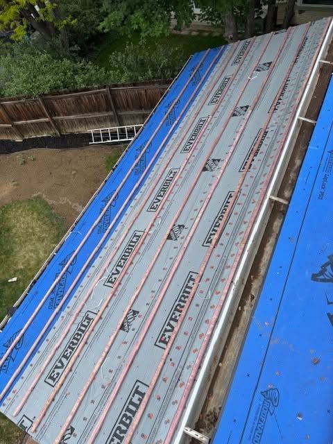 Blue-roof construction panels stacked diagonally beside a yard and wooden fence