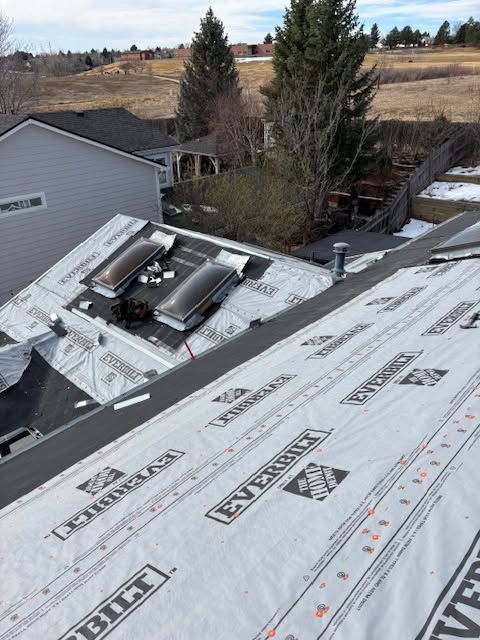 Rooftop with new white roofing underlayment and skylights, overlooking nearby houses and trees