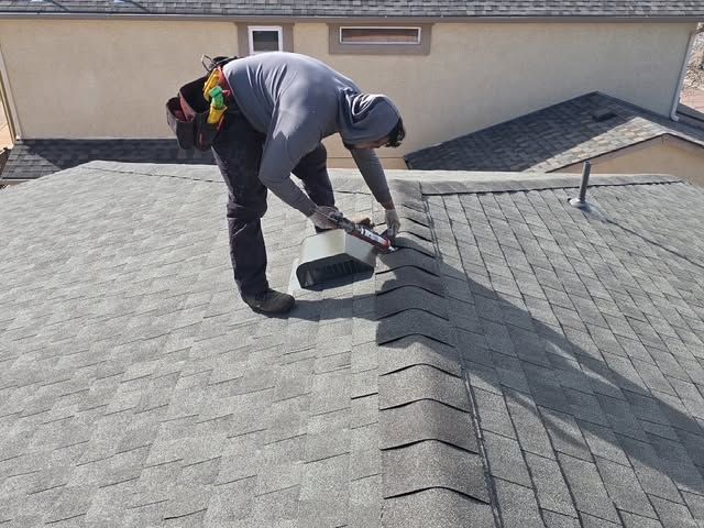 Worker repairing a gray shingle roof near a rooftop vent