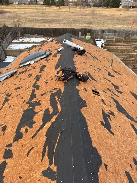 Partially stripped roof with black underlayment and scattered shingles at a construction site
