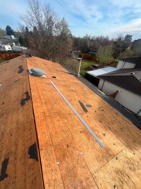 Roofer’s plywood roof deck with a vent pipe and metal flashing, seen over a residential neighborhood