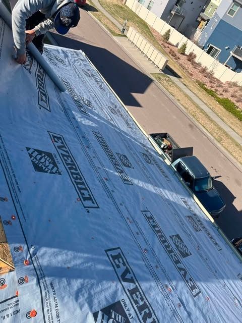 Roofing worker installing black roofing material on a sloped roof beside a residential street