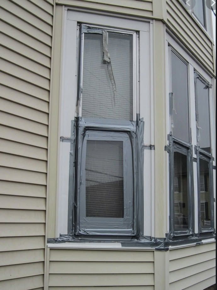 Damaged bay window on beige house exterior with cracked panes and peeling trim
