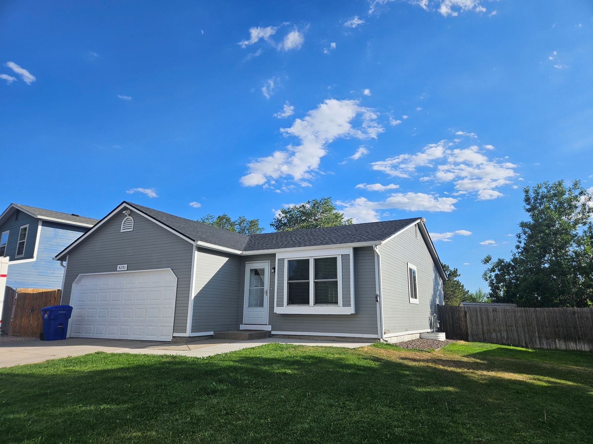 Small gray single-story house with garage, front lawn, and blue sky with clouds