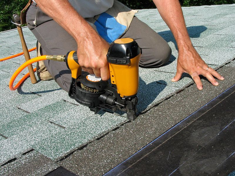 Worker using a nail gun to fasten roof shingles on a sloped roof