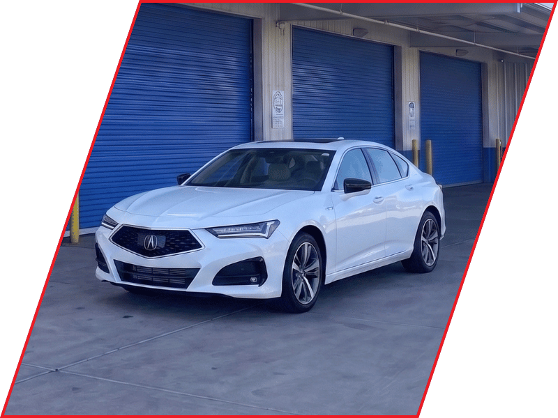 White Acura TLX luxury sedan parked outside an automotive service facility with blue garage doors