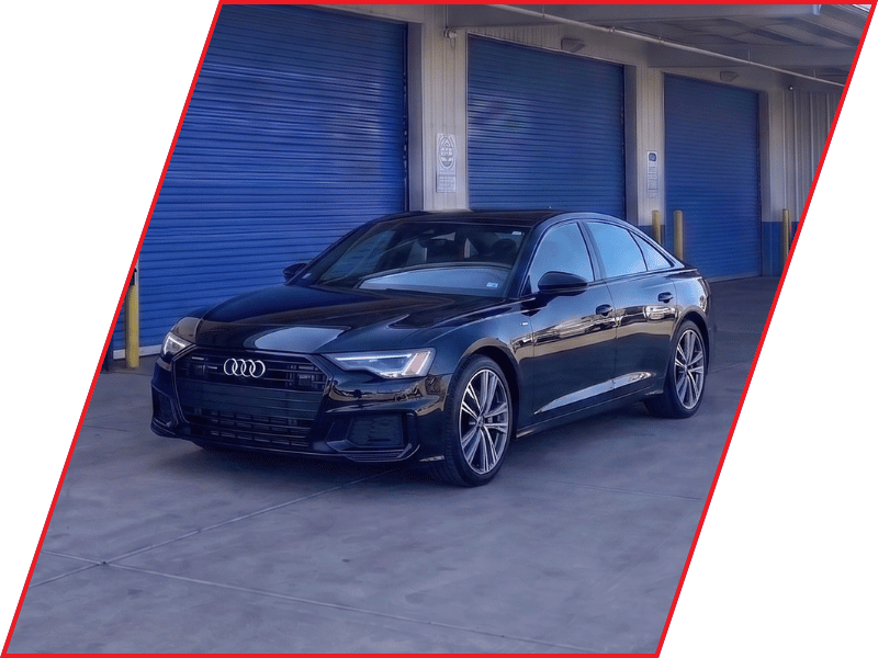 Black Audi A6 luxury sedan parked outside an automotive service facility with blue garage doors