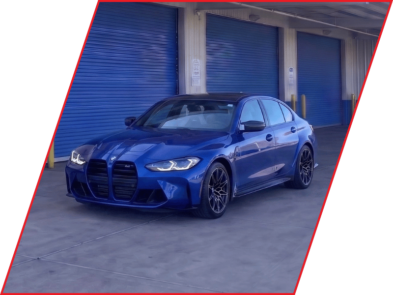 Blue BMW M3 sport sedan parked outside an automotive service facility with blue garage doors