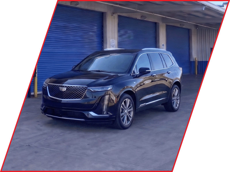 Black Cadillac XT6 luxury SUV parked outside an automotive service facility with blue garage doors
