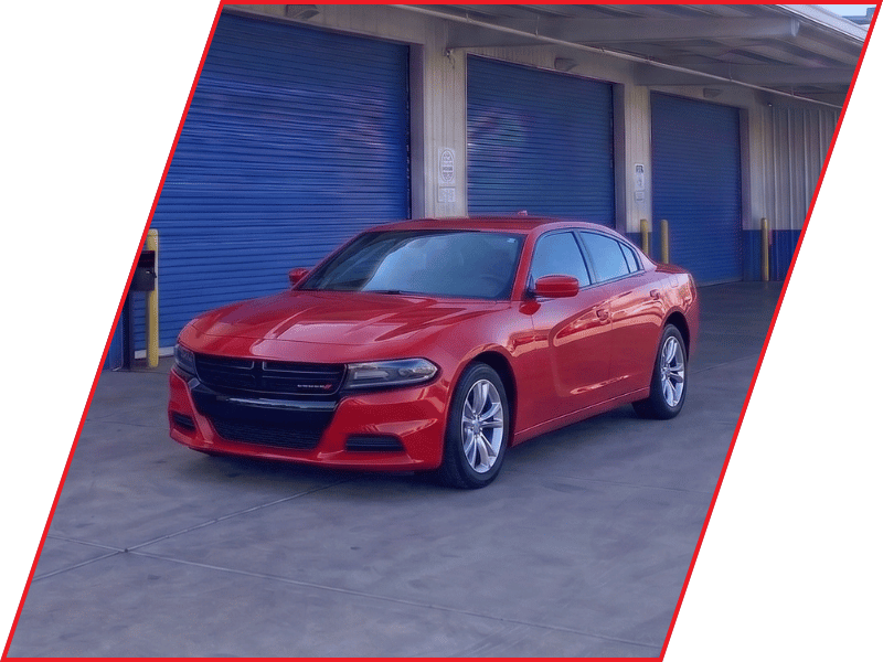 Red Dodge Charger sedan parked outside an automotive service facility with blue garage doors