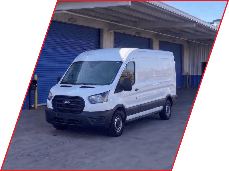 White Ford Transit cargo van parked outside an automotive service facility with blue garage doors