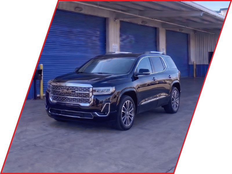 Black GMC Acadia SUV parked outside an automotive service facility with blue garage doors