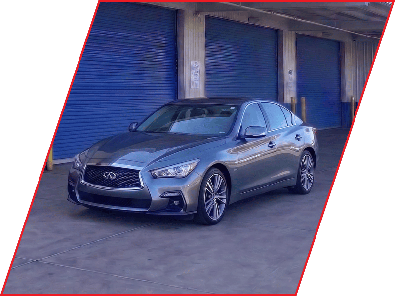 Gray Infiniti Q50 luxury sedan parked outside an automotive service facility with blue garage doors