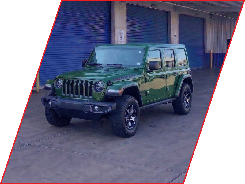 Green Jeep Wrangler Rubicon parked outside an automotive service facility with blue garage doors