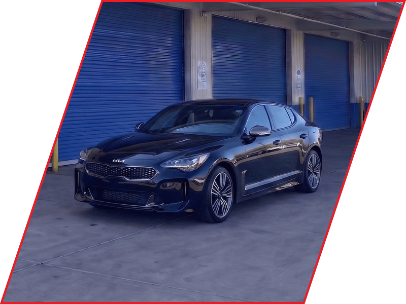 Black Kia Stinger sport sedan parked outside an automotive service facility with blue garage doors