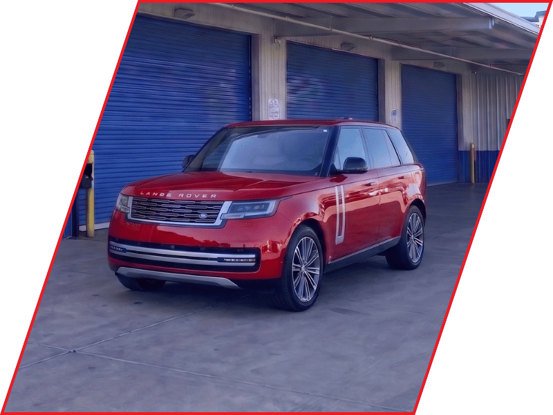 Red Land Rover Range Rover luxury SUV parked outside an automotive service facility with blue garage doors