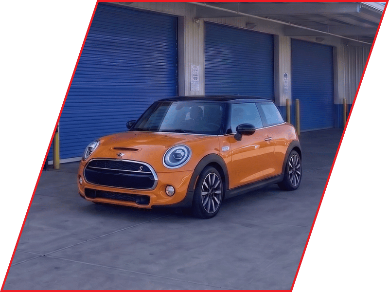 Orange MINI Cooper S hatchback parked outside an automotive service facility with blue garage doors