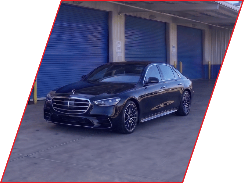 Black Mercedes-Benz S-Class luxury sedan parked outside an automotive service facility with blue garage doors