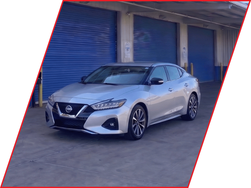 Silver Nissan Maxima sedan parked outside an automotive service facility with blue garage doors