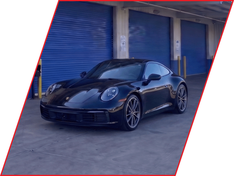Black Porsche 911 sports car parked outside an automotive service facility with blue garage doors