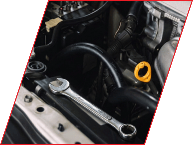 Wrench resting inside a vehicle engine bay near hoses and the oil dipstick