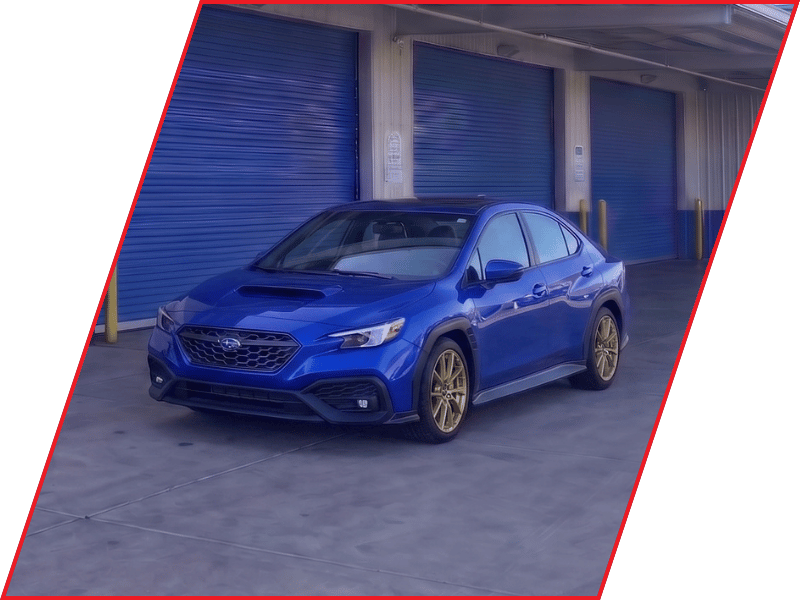 Blue Subaru WRX sport sedan parked outside an automotive service facility with blue garage doors
