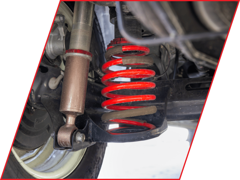 Close-up of a vehicle suspension system showing a red coil spring, shock absorber, and control arm
