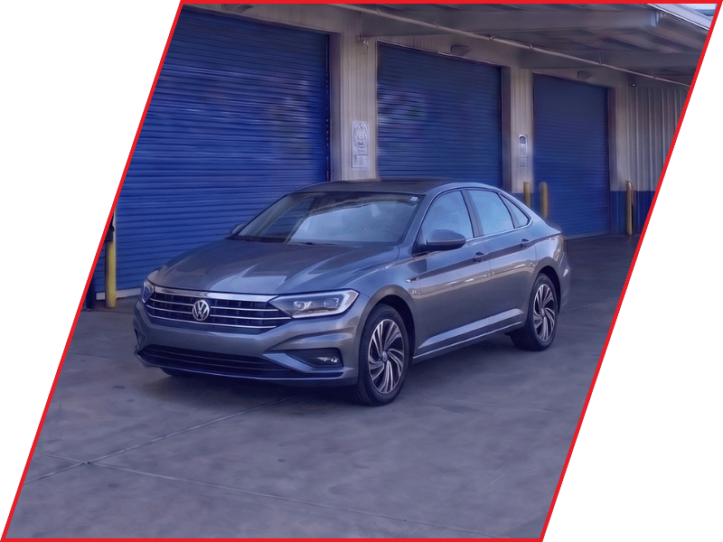 Gray Volkswagen Jetta sedan parked outside an automotive service facility with blue garage doors