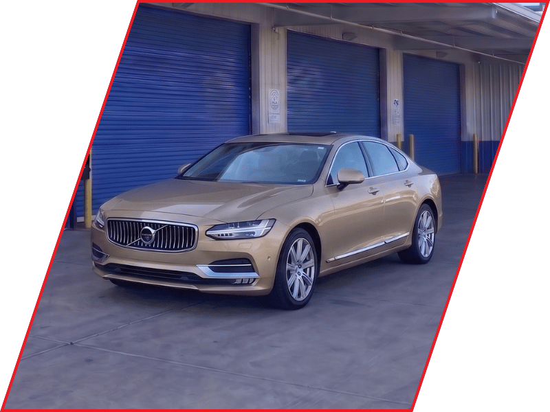 Gold Volvo S90 luxury sedan parked outside an automotive service facility with blue garage doors