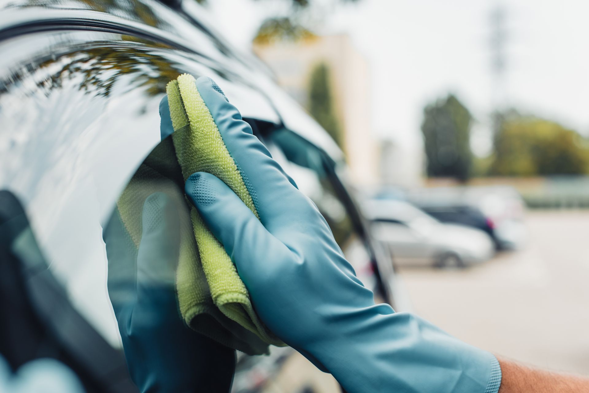 A gloved hand wipes down a black car surface with a green cloth.