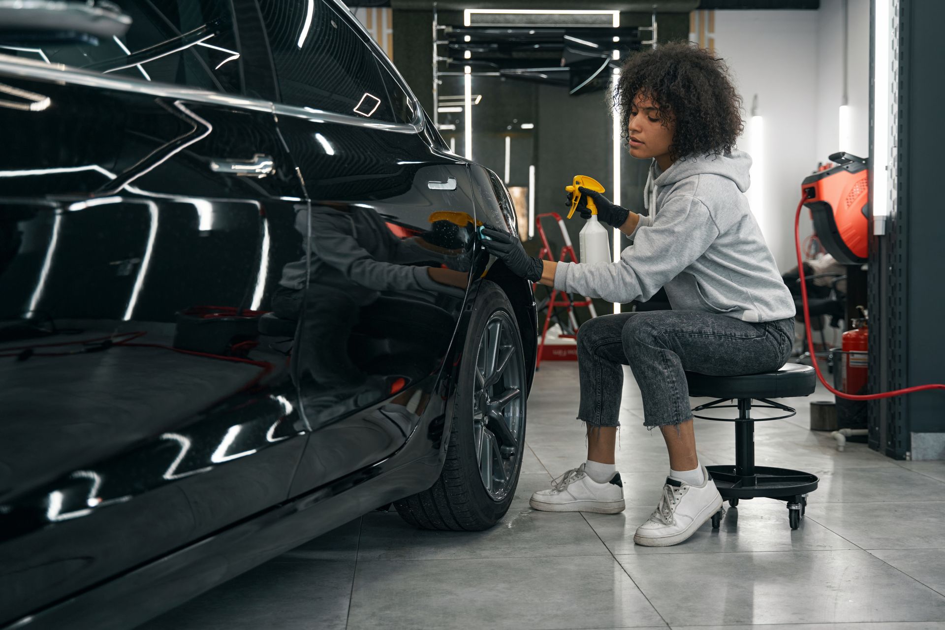Person spraying car with detailing product. They are seated in a garage.