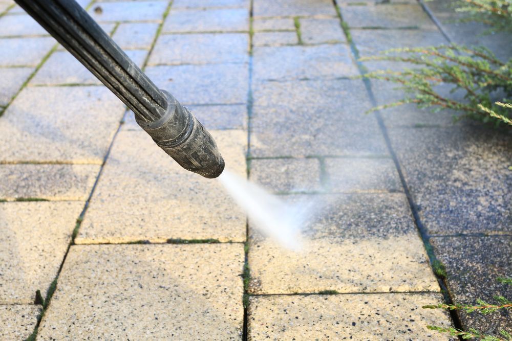 A person is using a high pressure washer to clean a brick walkway.