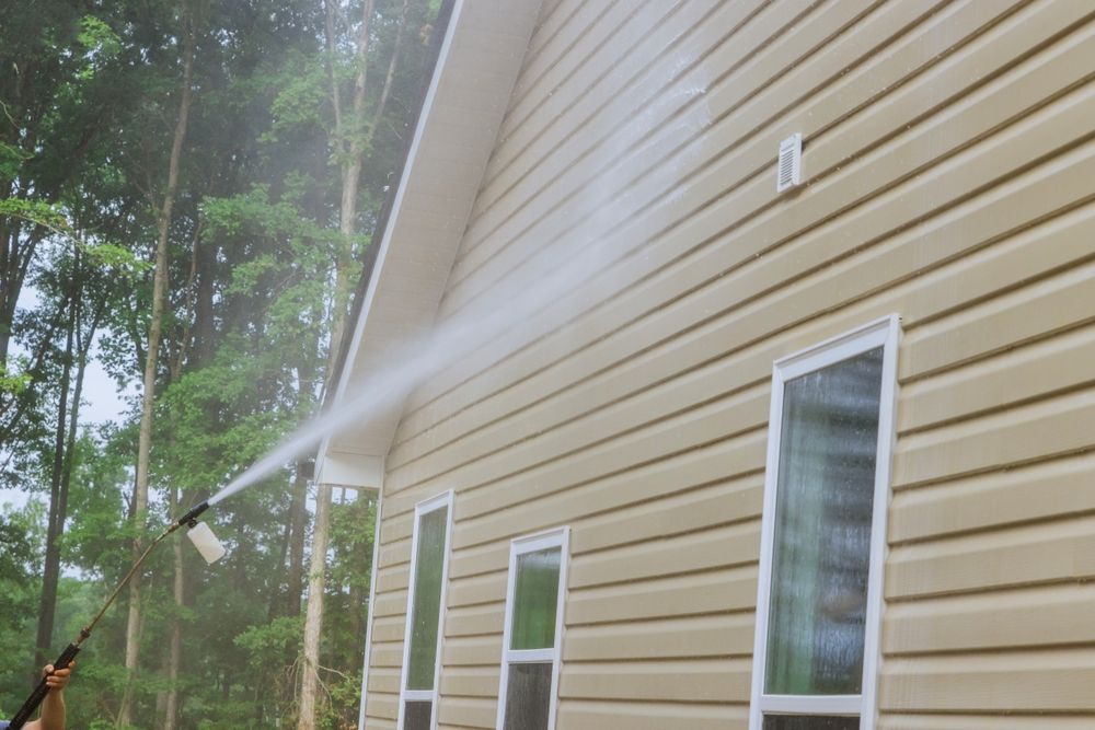 A man is using a pressure washer to clean the side of a house.