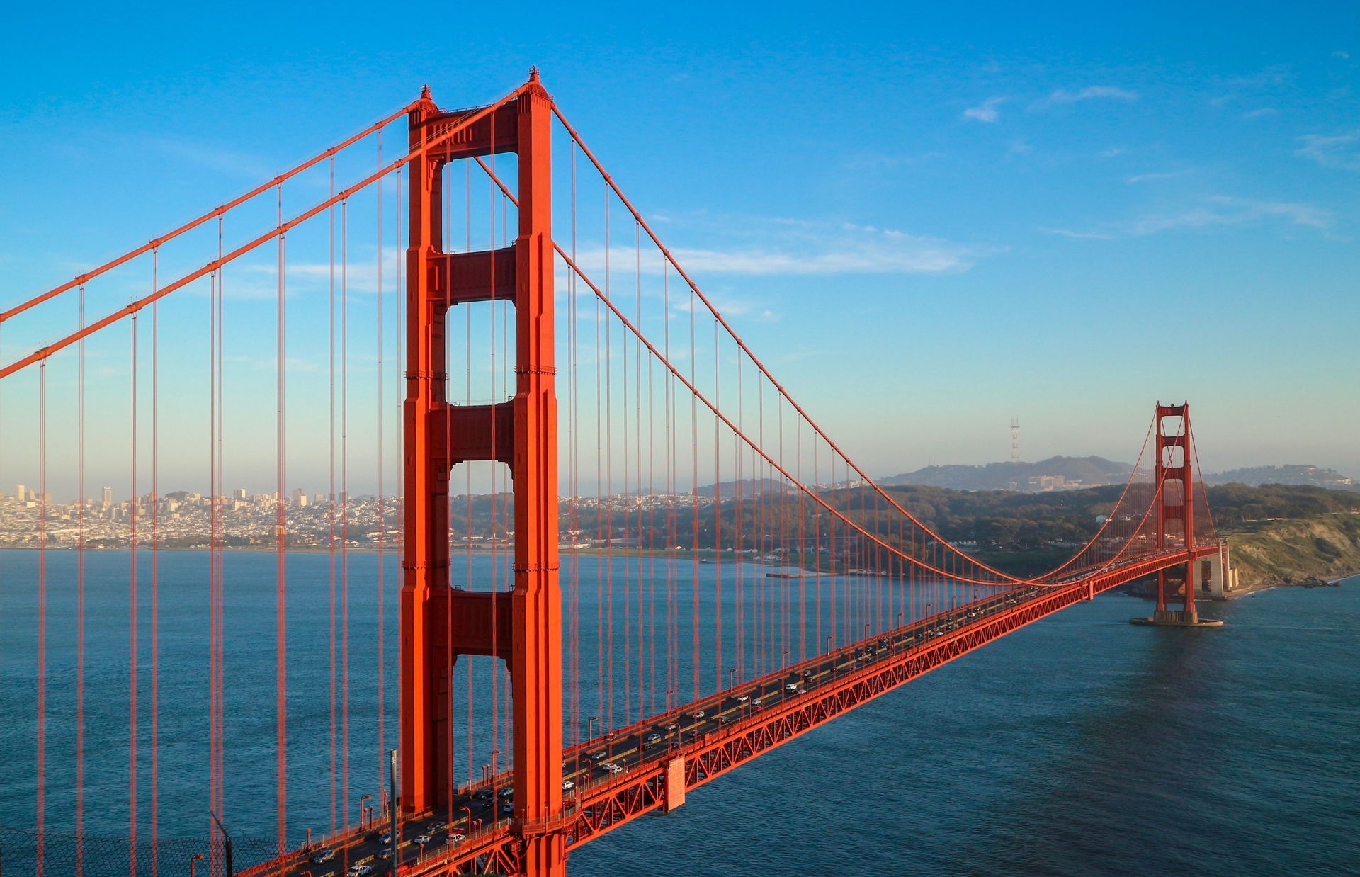 Golden Gate Bridge over San Francisco Bay on a clear day, with blue water and city skyline in the distance