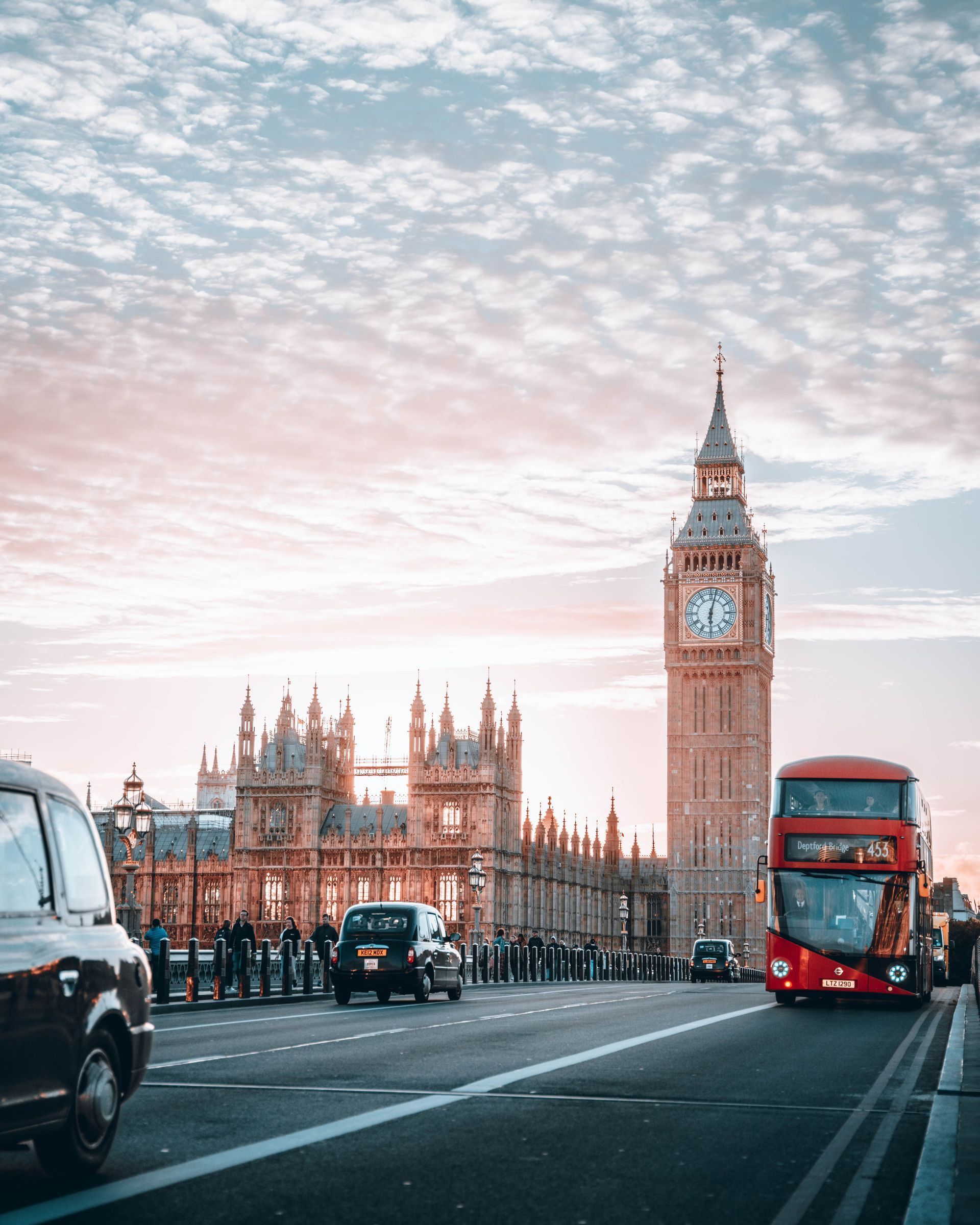 Big Ben and Parliament at dawn with traffic on a London bridge, including a red double-decker bus