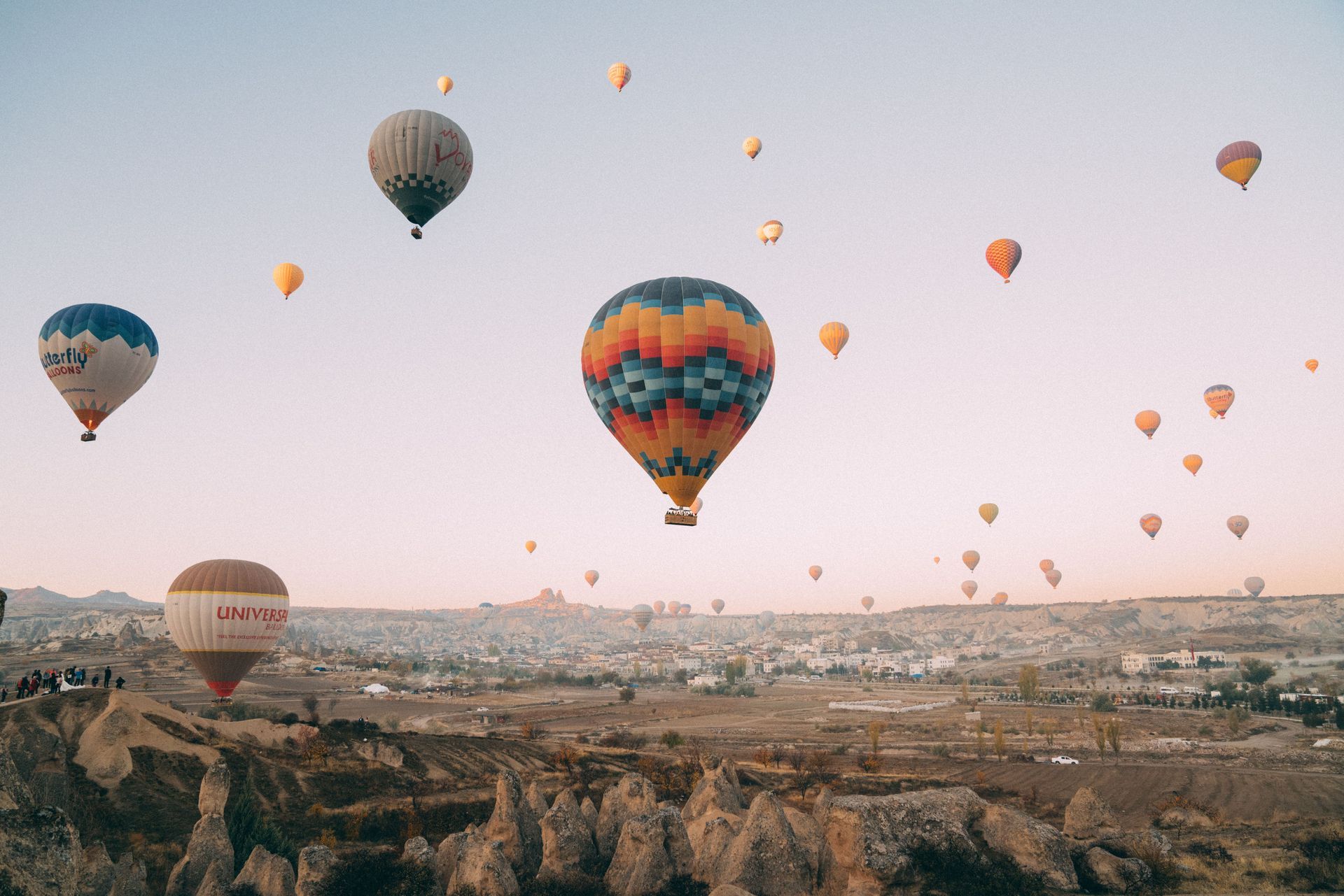 Hot air balloons floating over a rocky valley at sunrise, including a large colorful balloon in the center.