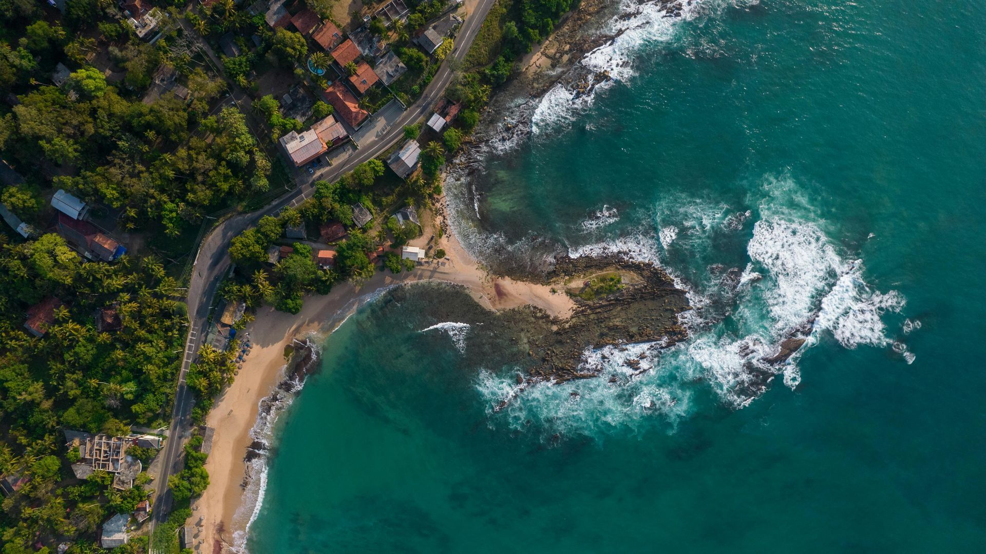 Aerial view of a rocky tropical cove with turquoise water, sandy beach, and lush green coastline.