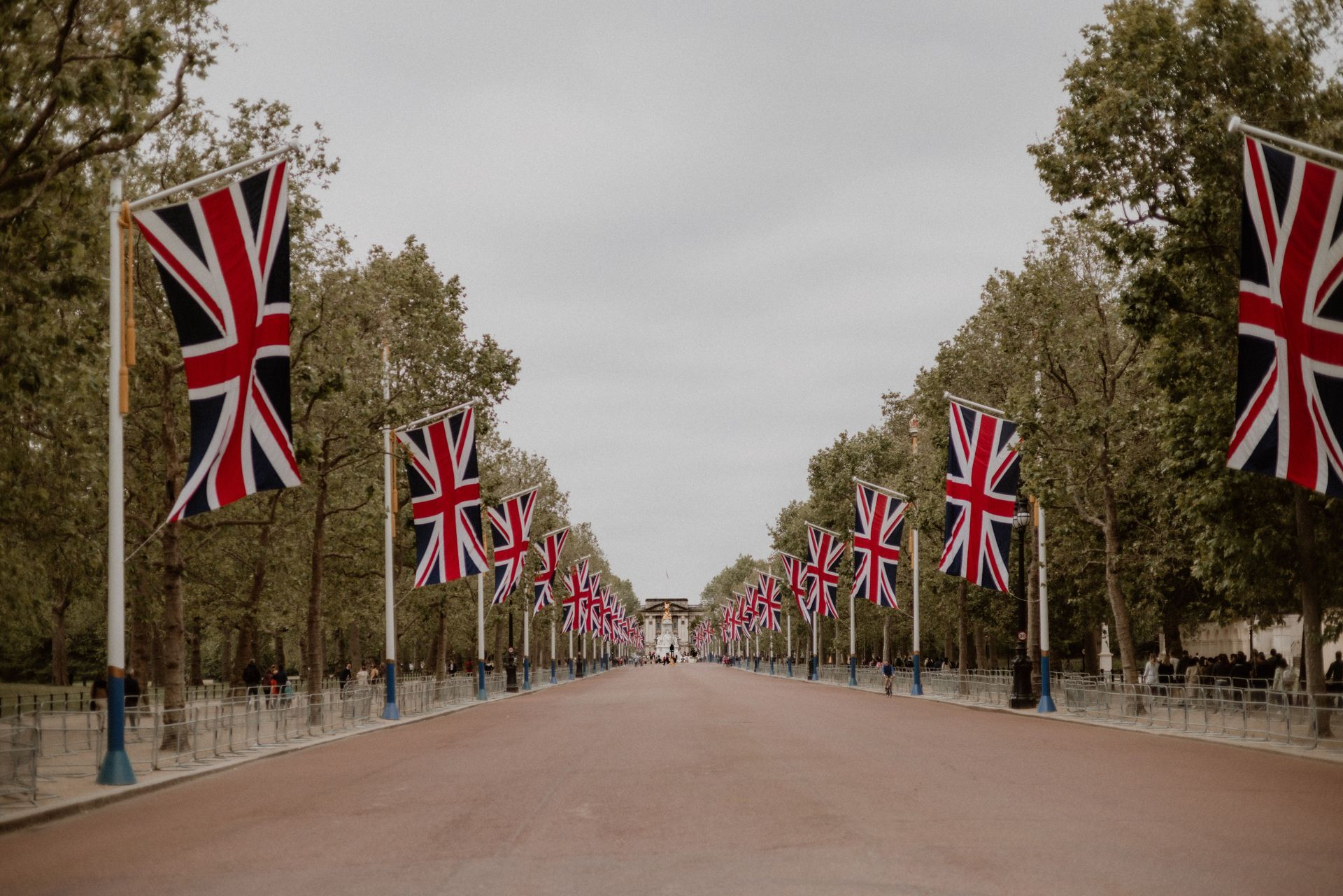 Tree-lined road with Union Jack flags on both sides under a gray sky