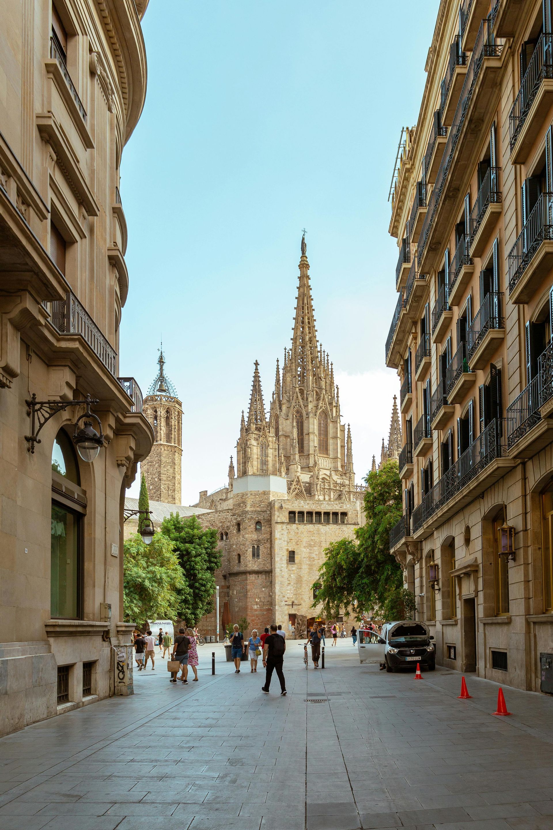 Cathedral street framed by ornate buildings, with pedestrians and a tall spired church in the distance