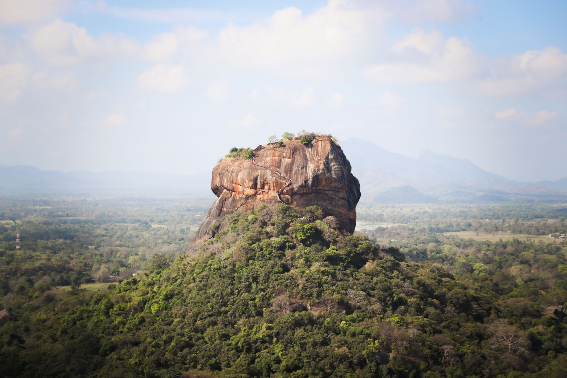 Sigiria rising above lush green forest under a hazy blue sky